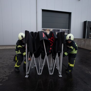 Vigili del fuoco di Ulm in Germania aprono un gazebo pieghevole 3x3m nero Ecotent personalizzato con scritta rossa durante un'emergenza