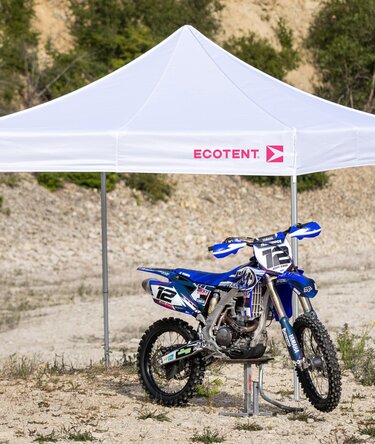 Gazebo bianco 3x3 m con logo Ecotent fuxia copre una moto da motocross blu nel deserto