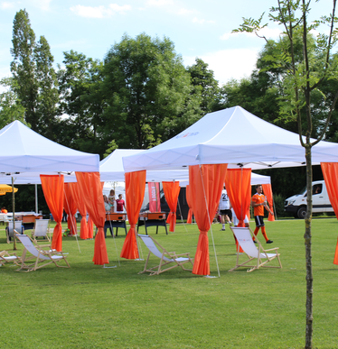 Serie di gazebo per eventi 6x3m bianchi con tende angolari arancioni personlizzati con logo IngDiba e bandiere a goccia bianche per evento all'aperto su un grande campo sportivo