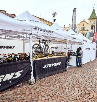 Il gazebo promozionale di Stevens Bikes è un gazebo pieghevole di 4x2 m di colore bianco. Le pareti laterali sono bianche e nere. Le biciclette sono posizionate sotto i gazebo pieghevoli.