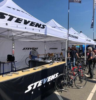White 3x3m event gazebo customised with Stevens bikes logo at bicycle sporting event with black half-height side walls with counter