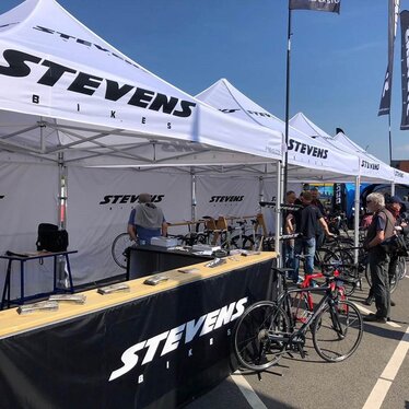 Weißer 3x3 m Eventzelt mit Stevens-Bikes-Logo für eine Radsportveranstaltung mit schwarzen halbhohen Seitenwänden und Theken
