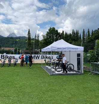 Weißer 6x3 Faltpavillon mit BMW Bike experience Schriftzug und Seitenwand auf einer Wiese mit Baum- und Bergkulisse 