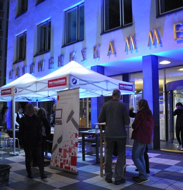 Weißes 3x3m Eventzelzelt mit Handwerkskammer-Logo und blauen Lichtern bei Nacht zum Schutz von Personen und Tischen bei einer Veranstaltung