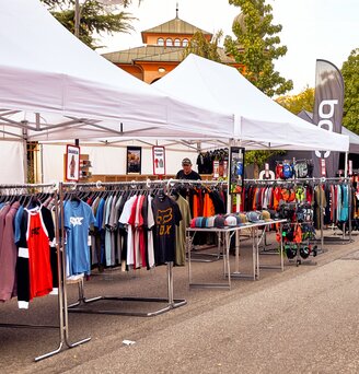 I gazebo promozionali bianche fungono come gazebo di vendita in occasione di un evento. Sotto i gazebo sono appese diverse magliette.