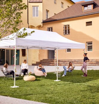 The 6x3 m folding gazebo serves as an outdoor canopy for a library. Young people sit under it.
