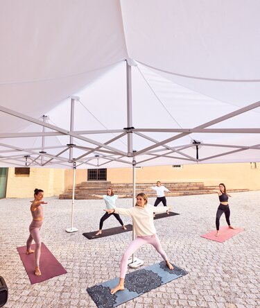 Gazebo Ecotent bianco 6x4m su gairdino davanti alla biblioteca di Bressanone utilizzato outdoor ripara le partecipanti al corso di yoga 