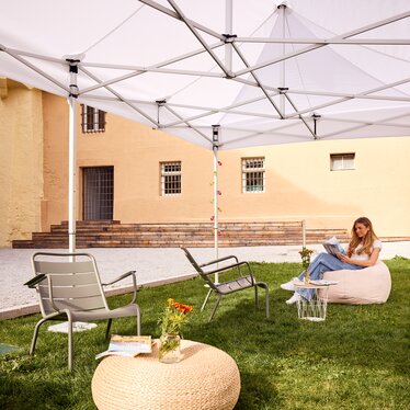 Gazebo Ecotent bianco 6x4m su gairdino davanti alla biblioteca di Bressanone utilizzato outdoor ripara dal sole una studentessa bionda che legge 