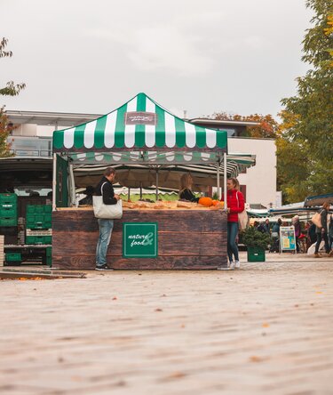 3x3 m Faltzelt auf dem Wochenmarkt. Der Faltpavillon ist vollflächig bedruckt, hat verschiedene Seitenwände und eine Theke. Er dient als Verkaufsstand für Obst und Gemüse.