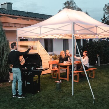 Gli amici festeggiano un barbecue e una festa in giardino sotto il gazebo da giardino. Il gazebo è decorato a festa con luci fiabesche.