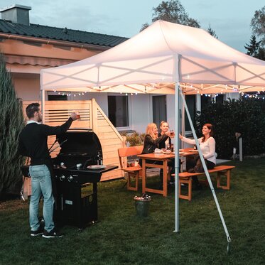 Gli amici festeggiano un barbecue e una festa in giardino sotto il gazebo da giardino. Il gazebo è decorato a festa con luci fiabesche.