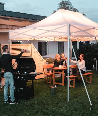 Gli amici festeggiano un barbecue e una festa in giardino sotto il gazebo da giardino. Il gazebo è decorato a festa con luci fiabesche.