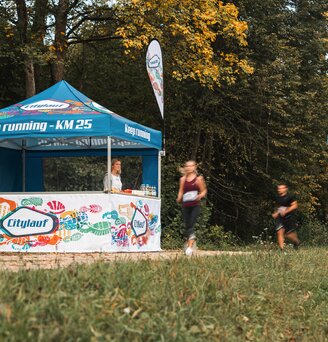 Il gazebo blu e bianca serve come stazione di rifornimento per la maratona. 2 atleti passano davanti al gazebo dell'evento.