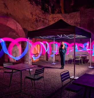 Il gazebo pieghevole nero si trova in un cortile. Una giovane donna si trova sotto di essa. Intorno al padiglione pieghevole ci sono strisce rosa e blu.