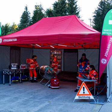 Gazebo per le emergenze 6x4 rosso con pareti laterali Rescue grige e due bandiere a goccia personalizzate con logo utilizzato per una simulazione di emergenzain fiera