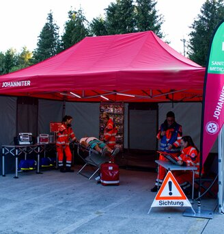 Gazebo per le emergenze 6x4 rosso con pareti laterali Rescue grige e due bandiere a goccia personalizzate con logo utilizzato per una simulazione di emergenzain fiera