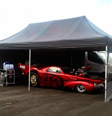Gazebo pieghevole per auto e motorsport 6x4 grigio scuro personalizzato con Flex fa da paddock a un'auto rossa. Ecotent