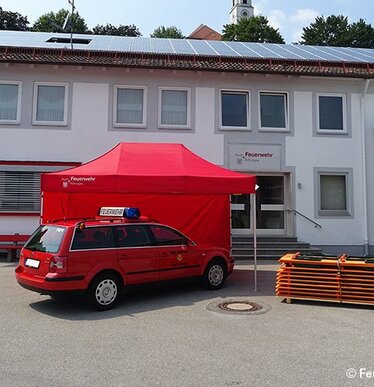 Gazebo 3x4,5 rosso per vigili del fuoco con una parete laterale rossa e scritta bianca personalizzata accanto a macchina dei vigili del fuoco e pila di tavoli e panche pieghevoli del brand RUKU1952
