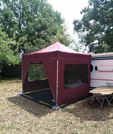 Gazebo pieghevole 3x3 da campeggio color bordeaux con teli laterali e pavimento in pvc davanti a un camper in un bosco