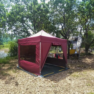 Gazebo pieghevole 3x3 da campeggio color bordeaux con teli laterali e pavimento in pvc in un camping