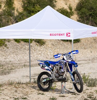 Gazebo bianco 3x3 m con logo Ecotent fuxia copre una moto da motocross blu nel deserto