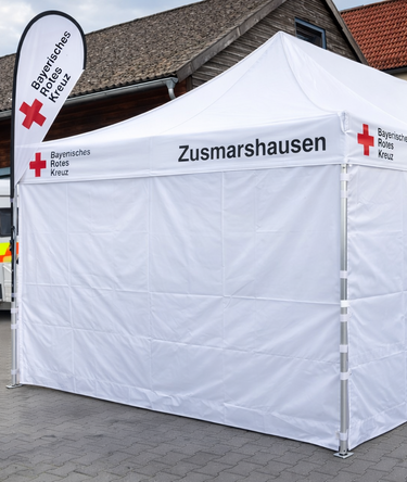Faltpavillon 8x4 m weiß mit geschlossenen Seitenwänden und Seitenwänden mit Fenster, personalisiert mit dem Logo vom Bayersischen Roten Kreuz.